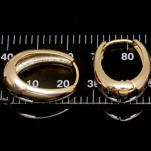 May include: Two gold hoop earrings, one measuring 20 mm and the other 50 mm in diameter, are displayed on a black surface with a ruler for scale.