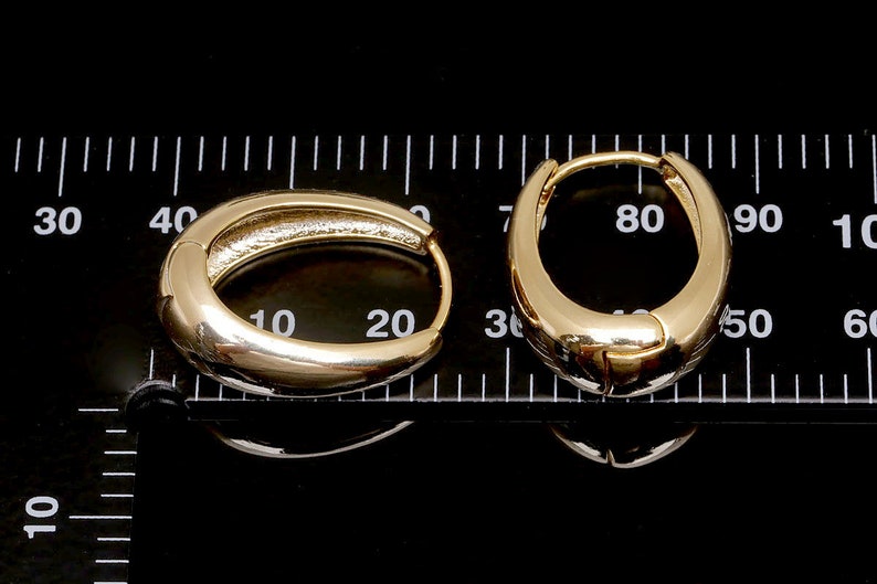 May include: Two gold hoop earrings, one measuring 20 mm and the other 50 mm in diameter, are displayed on a black surface with a ruler for scale.