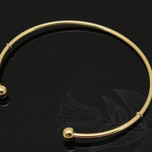 Könnte beinhalten: Ein goldenes Armreif-Armband mit zwei runden Kugelakzenten an den Enden.