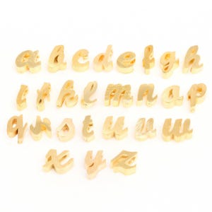 May include: Gold-colored metal alphabet letter charms in a cursive font. The letters are arranged in alphabetical order.