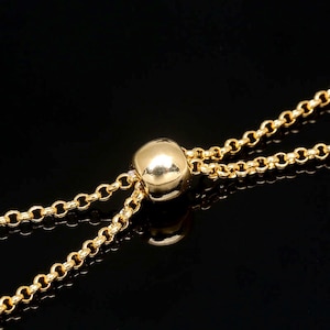 Op de afbeelding: Een gouden kettingarmband met een schuifknop. De ketting is gemaakt van kleine, ronde schakels en de kraal is glad en rond.