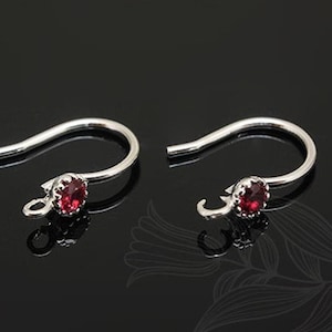 Puede incluir: Un par de ganchos para pendientes de plata con una pequeña piedra preciosa roja en el centro de cada gancho.