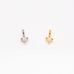 Puede incluir: Dos pequeños colgantes, uno plateado y otro dorado, cada uno con una gema rosa pálido. Las gemas son redondas y están engastadas en un engaste de cuatro puntas. Los colgantes están diseñados para ser usados como joyas.