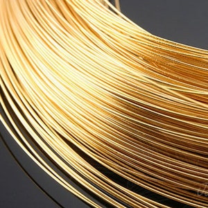 May include: A close-up of a spool of gold-colored wire. The wire is tightly wound and has a shiny finish.