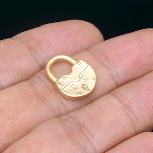 May include: A gold-colored padlock charm with a textured surface. The padlock is closed and has a small keyhole.