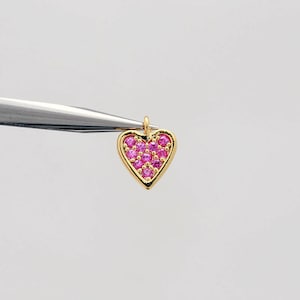 May include: A gold heart charm with pink gemstones. The charm is small and delicate, perfect for adding a touch of sparkle to jewellery.