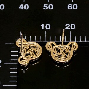 K&ouml;nnte beinhalten: Ein Paar goldfarbene Ohrstecker mit einem geometrischen Design in Form eines B&auml;renkopfes.