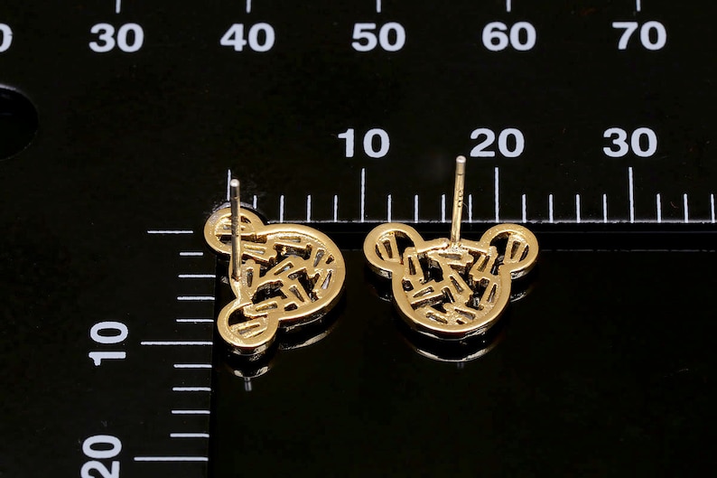 K&ouml;nnte beinhalten: Ein Paar goldfarbene Ohrstecker mit einem geometrischen Design in Form eines B&auml;renkopfes.