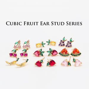 Op de afbeelding: Cubic Fruit Oorsteker Serie: Een set gouden oorbellen met verschillende fruitontwerpen met kleurrijke kubische zirkonia-stenen. De ontwerpen omvatten kersen, aardbeien, watermeloenen, druiven en citroenen.
