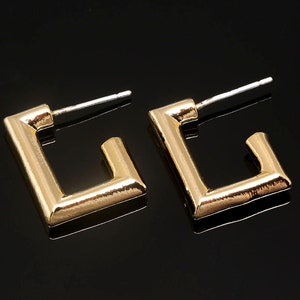 Puede incluir: Un par de pendientes de aro cuadrados de oro con un dise&ntilde;o sencillo. Los pendientes tienen un acabado pulido y est&aacute;n hechos de metal.