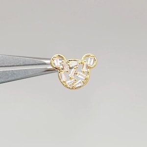 K&ouml;nnte beinhalten: Goldfarbener Ohrring in B&auml;renform mit klaren Baguette-f&ouml;rmigen Kristallen.