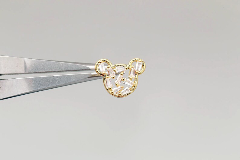 K&ouml;nnte beinhalten: Goldfarbener Ohrring in B&auml;renform mit klaren Baguette-f&ouml;rmigen Kristallen.