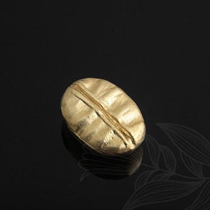 May include: A gold-coloured coffee bean charm, a small, detailed replica of a coffee bean.