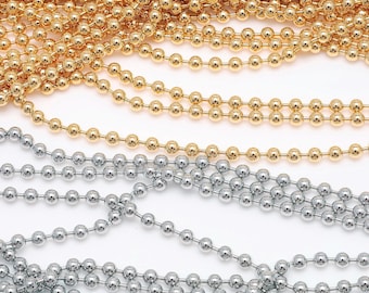 May include: Close-up of several strands of metallic bead chains in gold and silver. The beads are small and evenly spaced, creating a textured, reflective surface. The chains are arranged in parallel lines, showcasing the color variations and the light they reflect.
