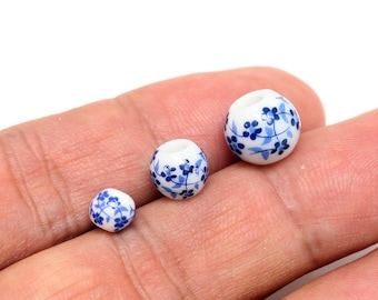 May include: Three white ceramic beads with blue floral designs. The beads are different sizes and are arranged in a row on a hand.