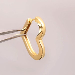 May include: A gold heart-shaped hoop earring. The earring is being held by a pair of pliers.