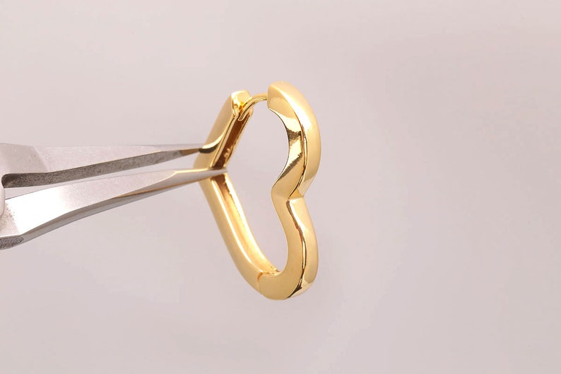 May include: A gold heart-shaped hoop earring. The earring is being held by a pair of pliers.