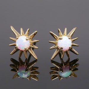 May include: A pair of gold starburst earrings with iridescent white opal stones in the centre.