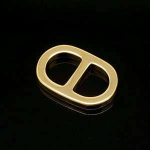 May include: A gold-colored metal ring with a rounded shape, resembling a figure eight. The ring has a smooth, polished finish.