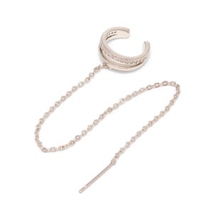 May include: A silver-toned ear cuff featuring a double-band design with embedded clear stones. A delicate silver chain connects the ear cuff to a straight post, creating a linked earring piece with a polished metallic finish and clear accents.