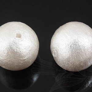 May include: Two white faux pearl beads with a hole in the center for stringing. The beads have a textured surface.