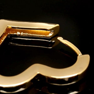 May include: Gold heart-shaped hoop earrings. The earrings are made of a smooth, shiny metal.