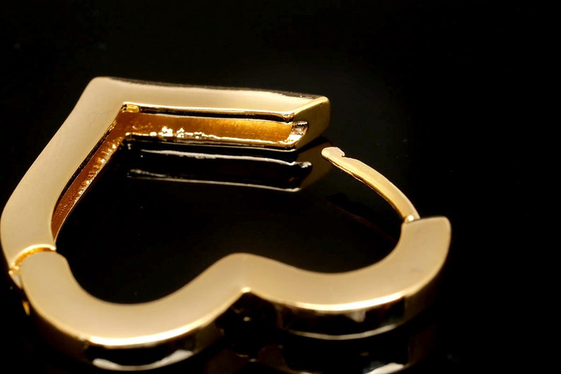 May include: Gold heart-shaped hoop earrings. The earrings are made of a smooth, shiny metal.