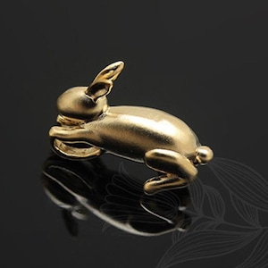 Puede incluir: Una figurita de conejo de color dorado, tumbada de lado con la cabeza apoyada en las patas delanteras. La figurita est&aacute; hecha de un metal liso y brillante y tiene un aspecto realista.