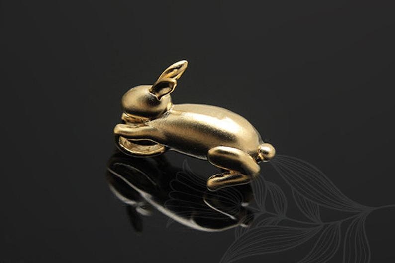 Puede incluir: Una figurita de conejo de color dorado, tumbada de lado con la cabeza apoyada en las patas delanteras. La figurita est&aacute; hecha de un metal liso y brillante y tiene un aspecto realista.