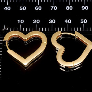 May include: A pair of gold heart-shaped hoop earrings. The earrings are made of a thick, shiny metal and have a smooth finish.