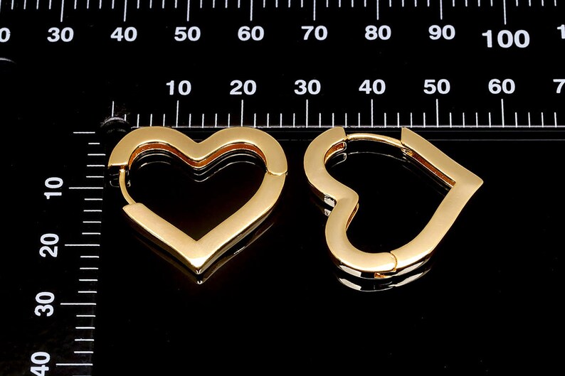 May include: A pair of gold heart-shaped hoop earrings. The earrings are made of a thick, shiny metal and have a smooth finish.