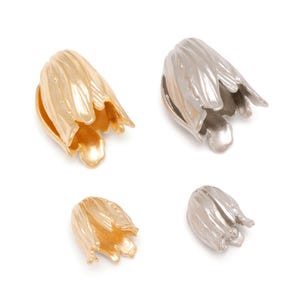 May include: Four metal bead caps shaped like tulip flowers, arranged in two pairs of different sizes. Two caps are gold-toned and two are silver-toned, each featuring a textured, petal-like design with a hollow centre for jewellery making.