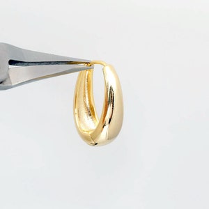 May include: A pair of gold hoop earrings being held by a pair of pliers.