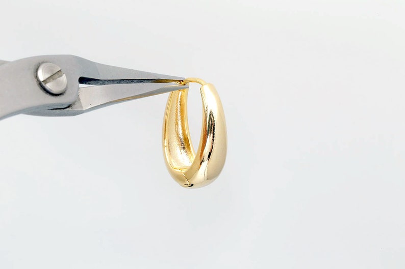 May include: A pair of gold hoop earrings being held by a pair of pliers.
