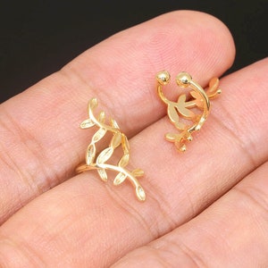 Könnte beinhalten: Zwei goldene Blatt-Ohrringe. Die Ohrringe sind aus dünnem Metall gefertigt und haben ein filigranes Design. Ohrringe sind ein beliebtes Modeaccessoire.