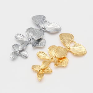 May include: Two sets of three dimensional flower charms. One set is gold and the other is silver. Each charm has a hole for attaching to a necklace or bracelet.