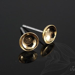 May include: Two gold-toned earring posts with a round, slightly domed top. The posts are made of metal and have a silver-toned finish.