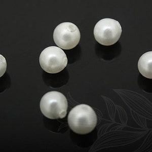 May include: Eight white pearl beads, each with a smooth, glossy finish. The beads are arranged in a scattered pattern on a black surface.