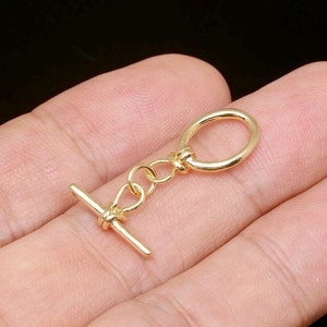 Puede incluir: Cierre de palanca de metal dorado con un anillo redondo y una barra en forma de T.