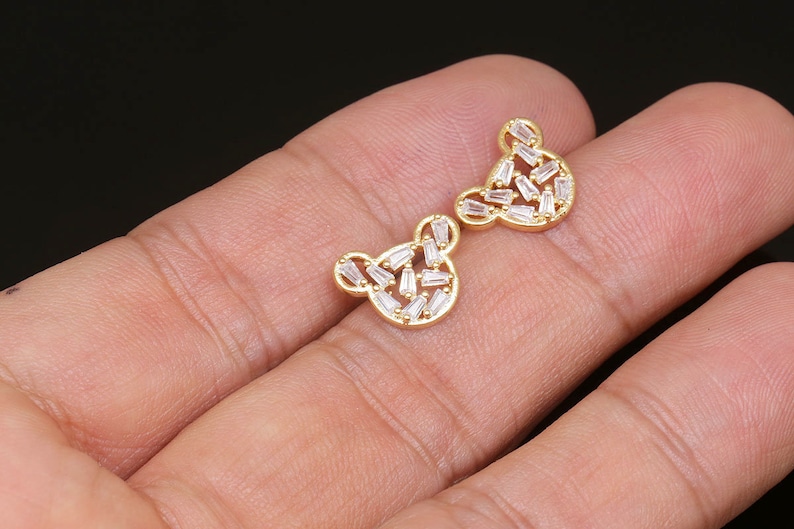 K&ouml;nnte beinhalten: Ein Paar goldfarbene Ohrringe in B&auml;renform mit klaren Zirkonia-Steinen.