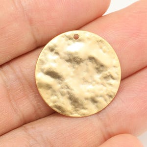 Puede incluir: Un colgante redondo de metal dorado con textura martillada y un pequeño agujero en la parte superior para colgar.