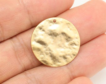Puede incluir: Un colgante redondo de metal dorado con textura martillada y un pequeño agujero en la parte superior para colgar.