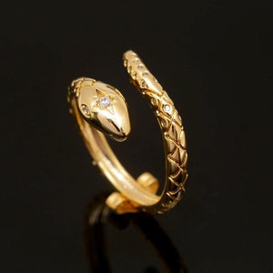Könnte beinhalten: Ein goldener Schlangenring mit einem einzelnen Diamanten auf dem Kopf der Schlange. Die Schlange ist um den Ringband gewickelt.
