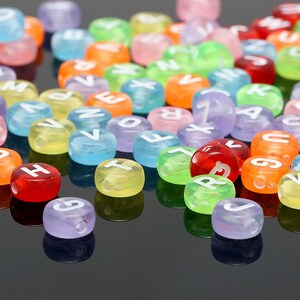 May include: A collection of colorful plastic alphabet beads with white letters. The beads are scattered on a black surface.