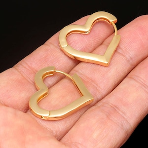 May include: A pair of gold heart-shaped hoop earrings. The earrings are open and have a smooth finish.