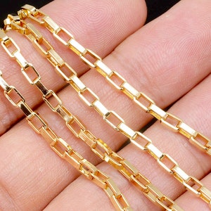 May include: Four gold chains with a box link design. The chains are laid out in a row on a hand.