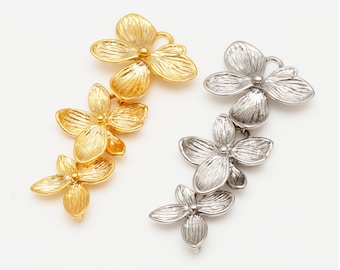 May include: Two floral-shaped jewelry components. One is gold-toned, the other is silver-toned. Each component features three flowers connected in a vertical arrangement. The flowers have detailed petal designs and are set against a white background.