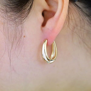 May include: Gold hoop earrings with a smooth, rounded finish. The earrings are worn in a person's ear.