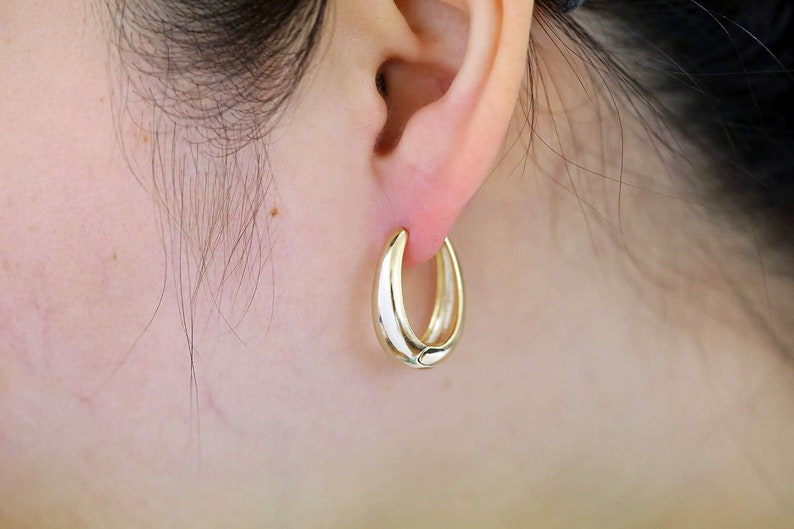 May include: Gold hoop earrings with a smooth, rounded finish. The earrings are worn in a person's ear.