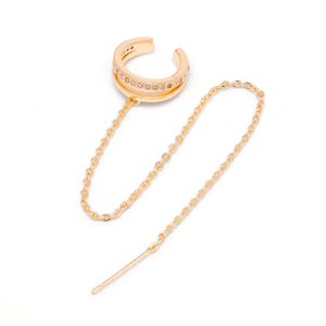 May include: A gold-toned ear cuff featuring a double-band design with a row of small clear stones embedded in the upper band. A delicate gold-toned chain connects the ear cuff to a thin, straight post earring, creating a linked jewelry piece.